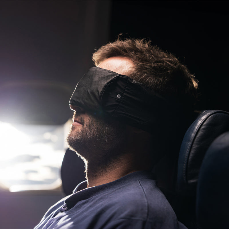 Man wearing sleep mask, asleep while sitting next to a very bright window